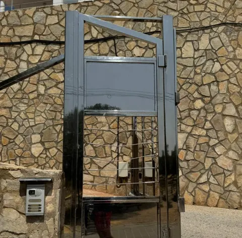 Puerta peatonal de acero inoxidable pulido junto a un muro de piedra