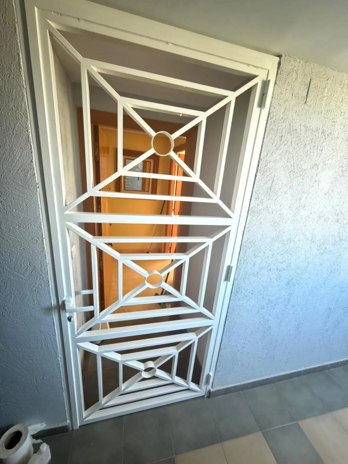 Puerta de reja blanca con diseño geométrico de rombos y círculos en la entrada de una vivienda